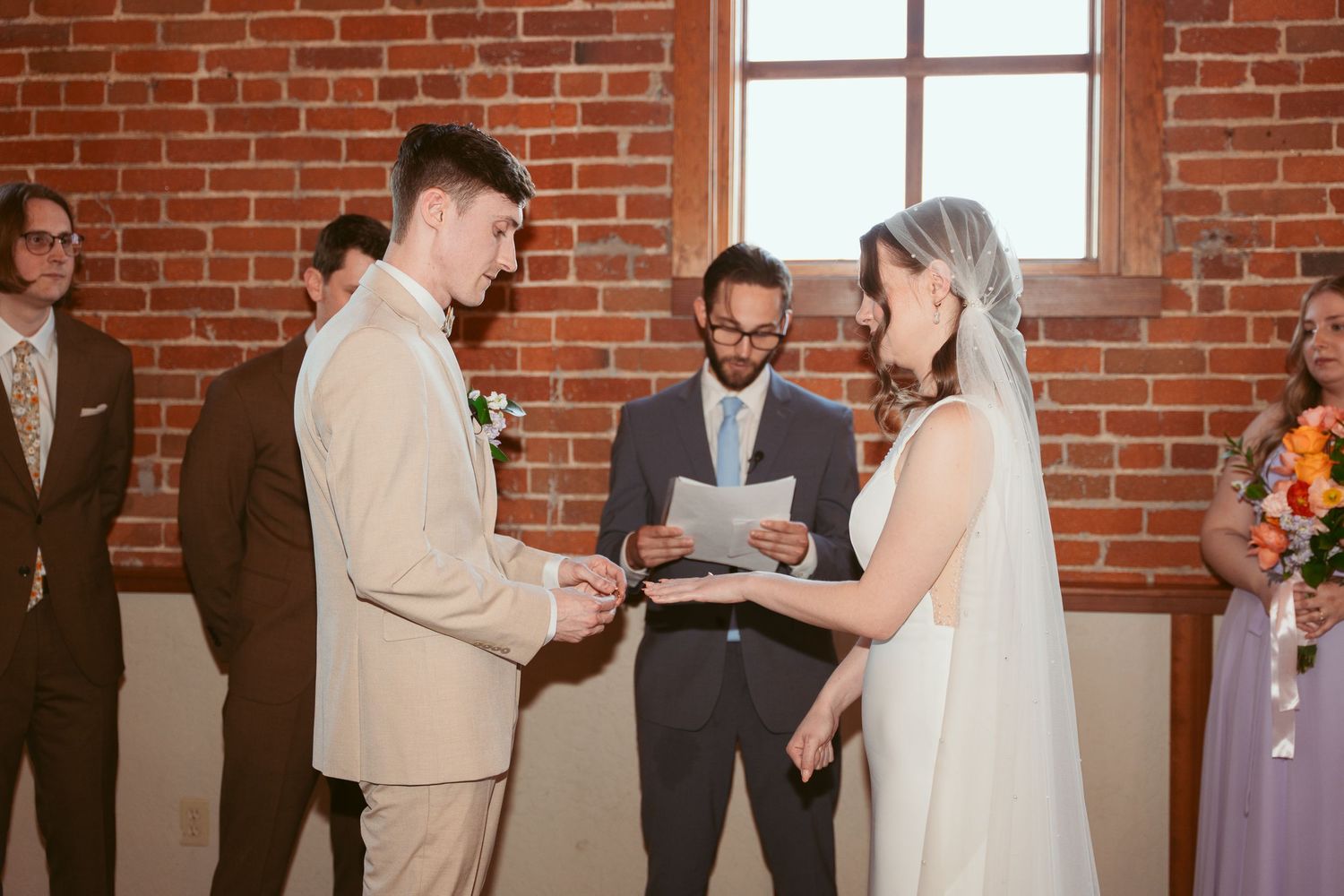 Couple exchanging vows during intimate wedding ceremony in industrial-style venue with exposed brick walls.