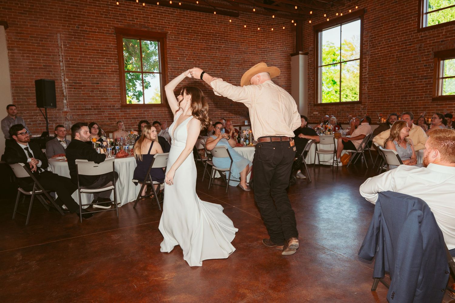 Wedding celebration with guests dancing under string lights in a charming brick-walled venue.
