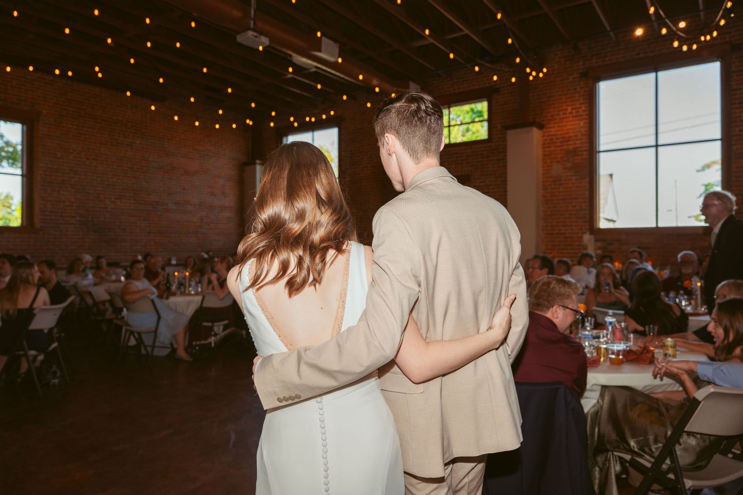 Wedding celebration in an industrial-style venue with exposed brick and string lights.