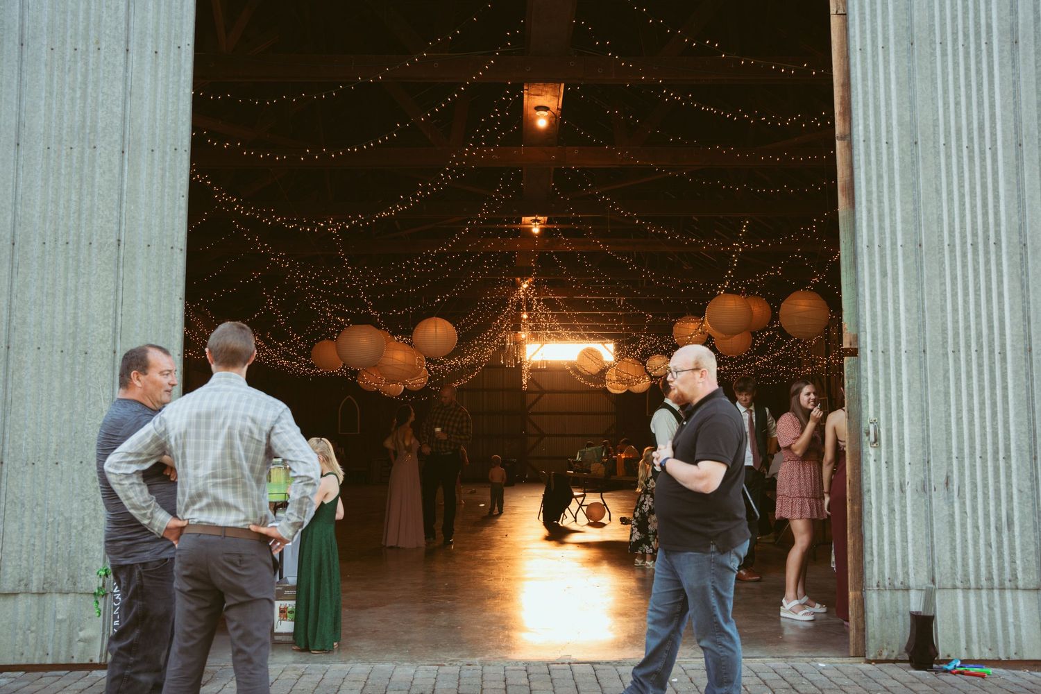 People dancing inside a barn venue decorated with warm lighting and white columns.