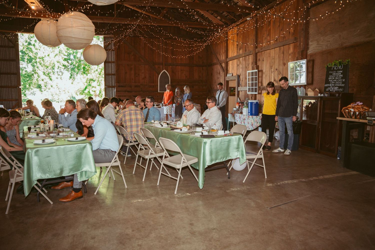 Wedding reception setup in a barn with twinkle lights and mint green table linens.