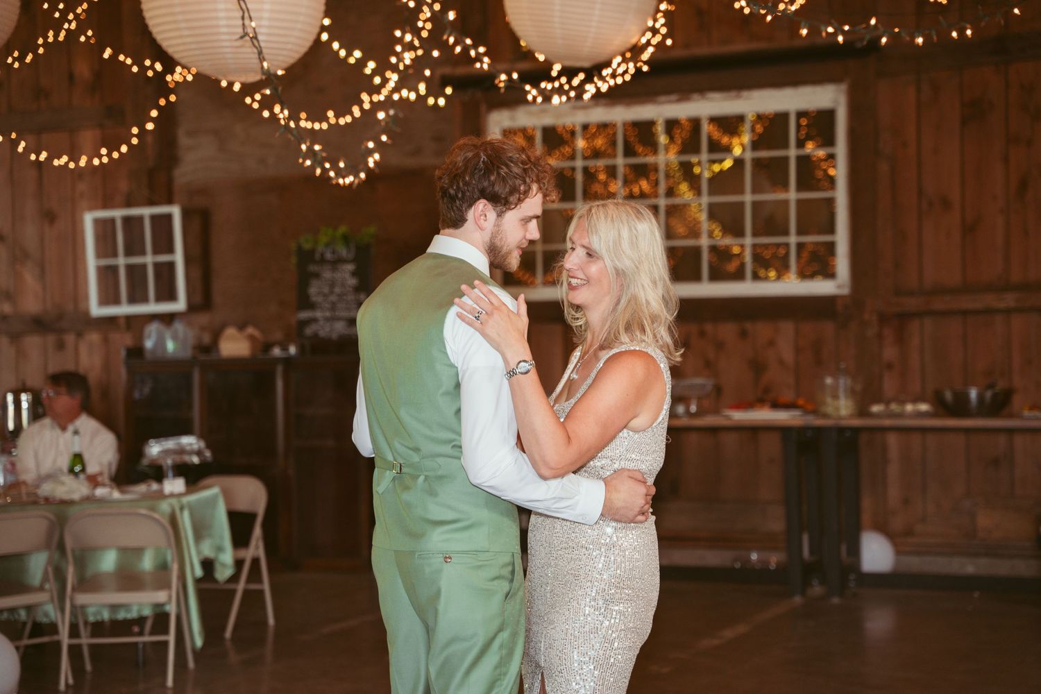 Romantic dance moment captured in rustic barn with twinkling lights and elegant decor.