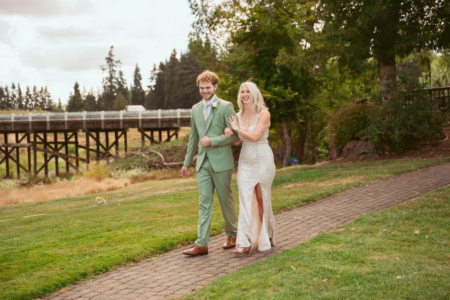 Wedding couple strolling along a brick path with trees and fencing in the background.