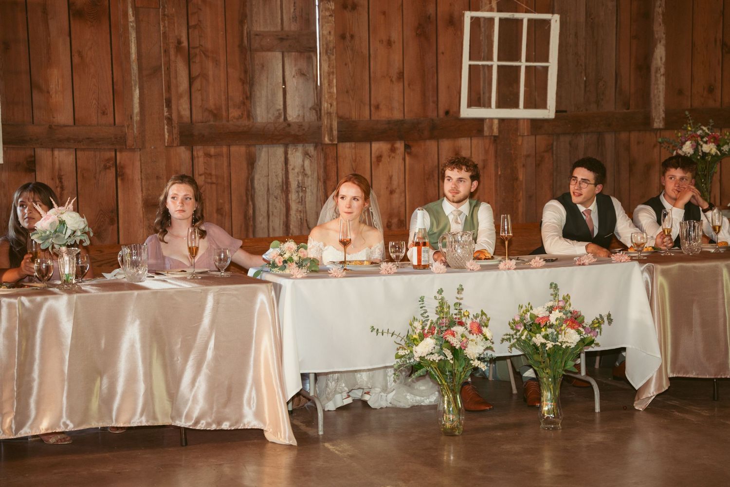 Wedding reception tables arranged in a rustic barn with white tablecloths and floral centerpieces.