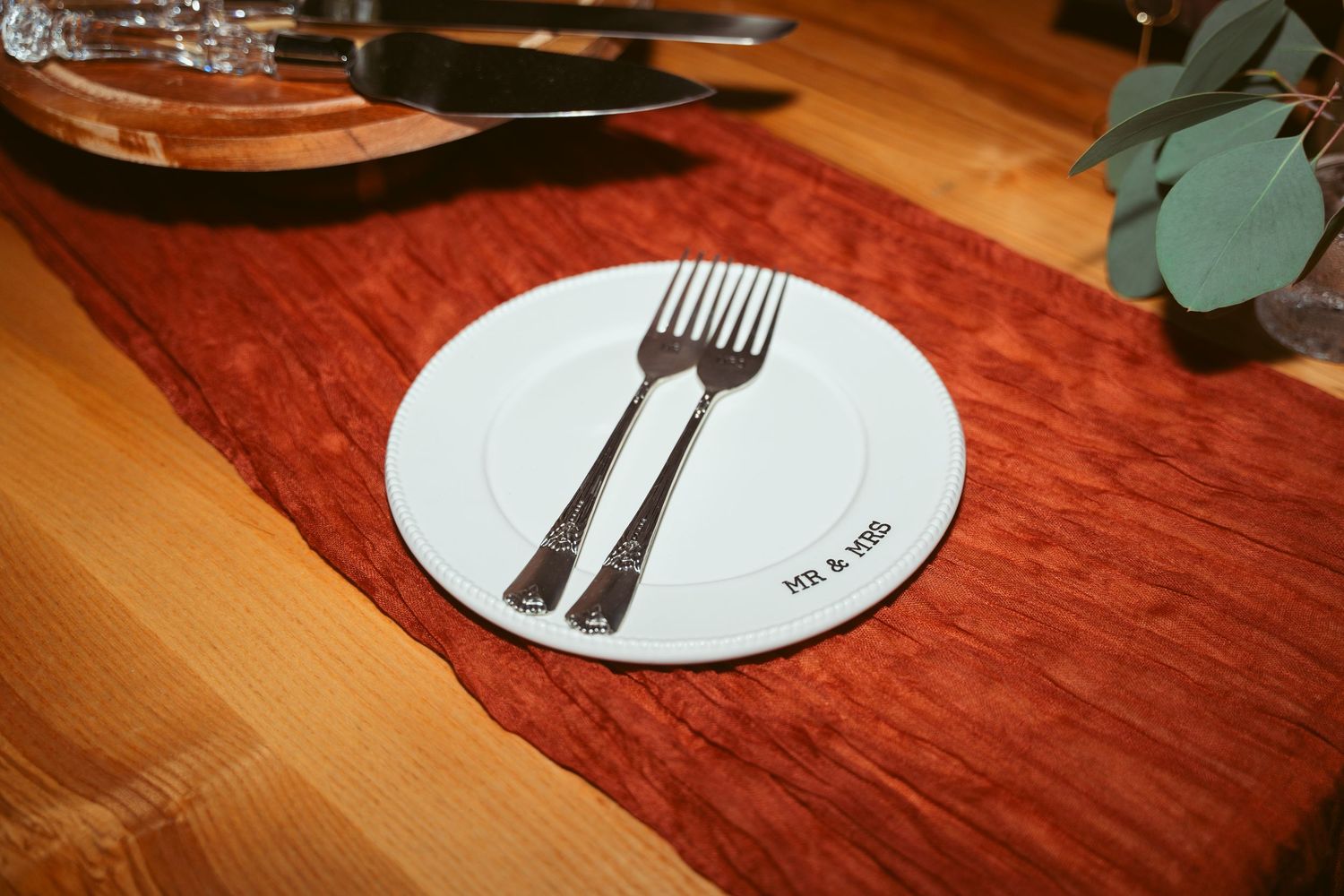 White plate with fork illustration on red table runner against wooden surface.