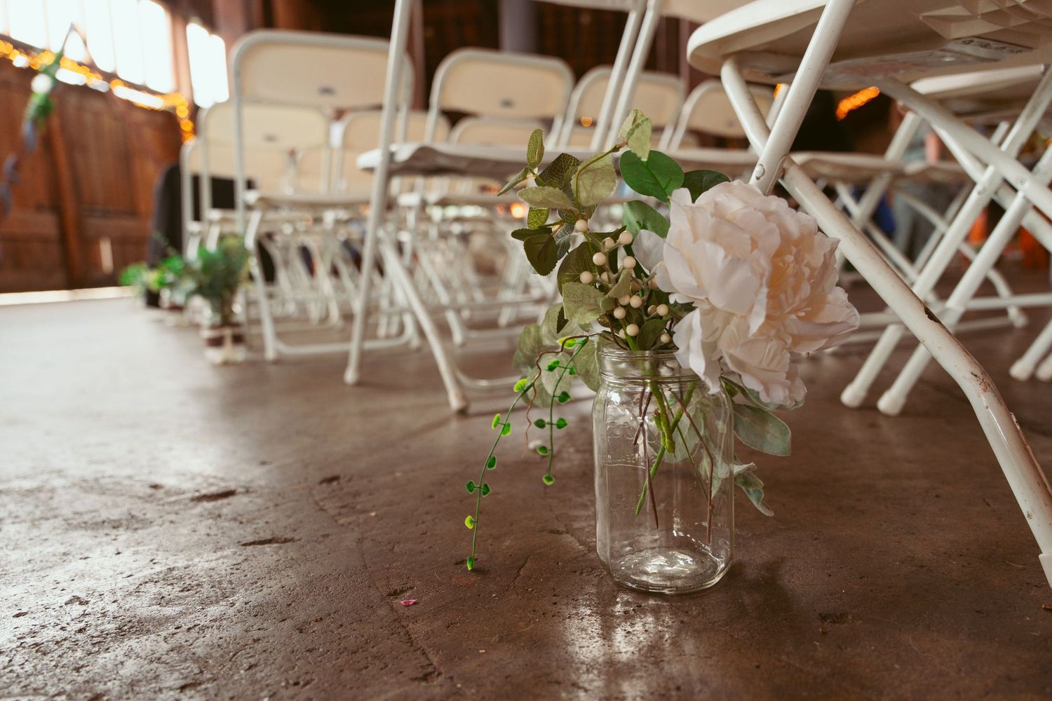 White folding chairs arranged for wedding ceremony with wooden floor and rustic details.