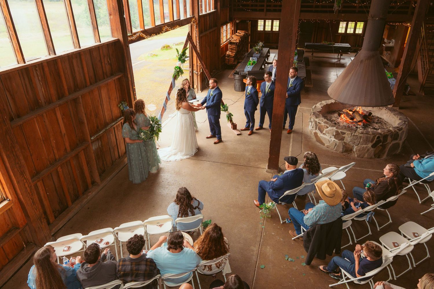 Wedding reception setup in rustic barn venue with string lights and wooden architecture.