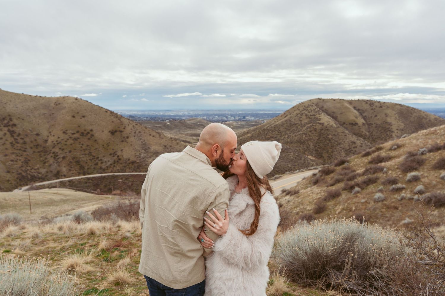 A romantic couple embraces against a dramatic desert mountain landscape.