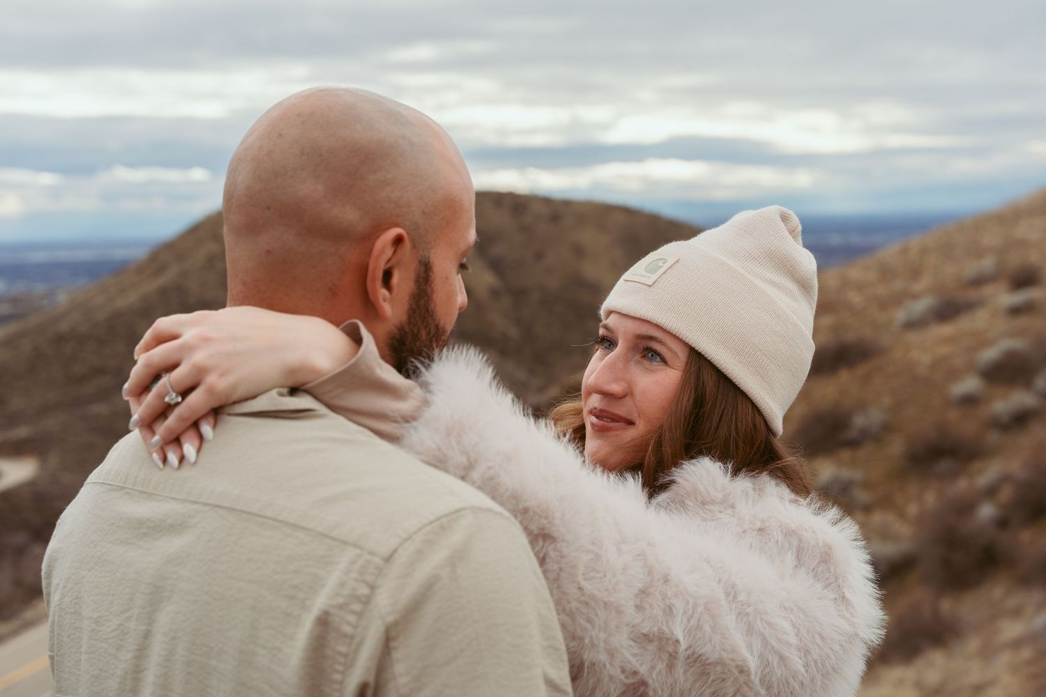 A couple shares an intimate moment while standing on a mountain overlook during an overcast day.