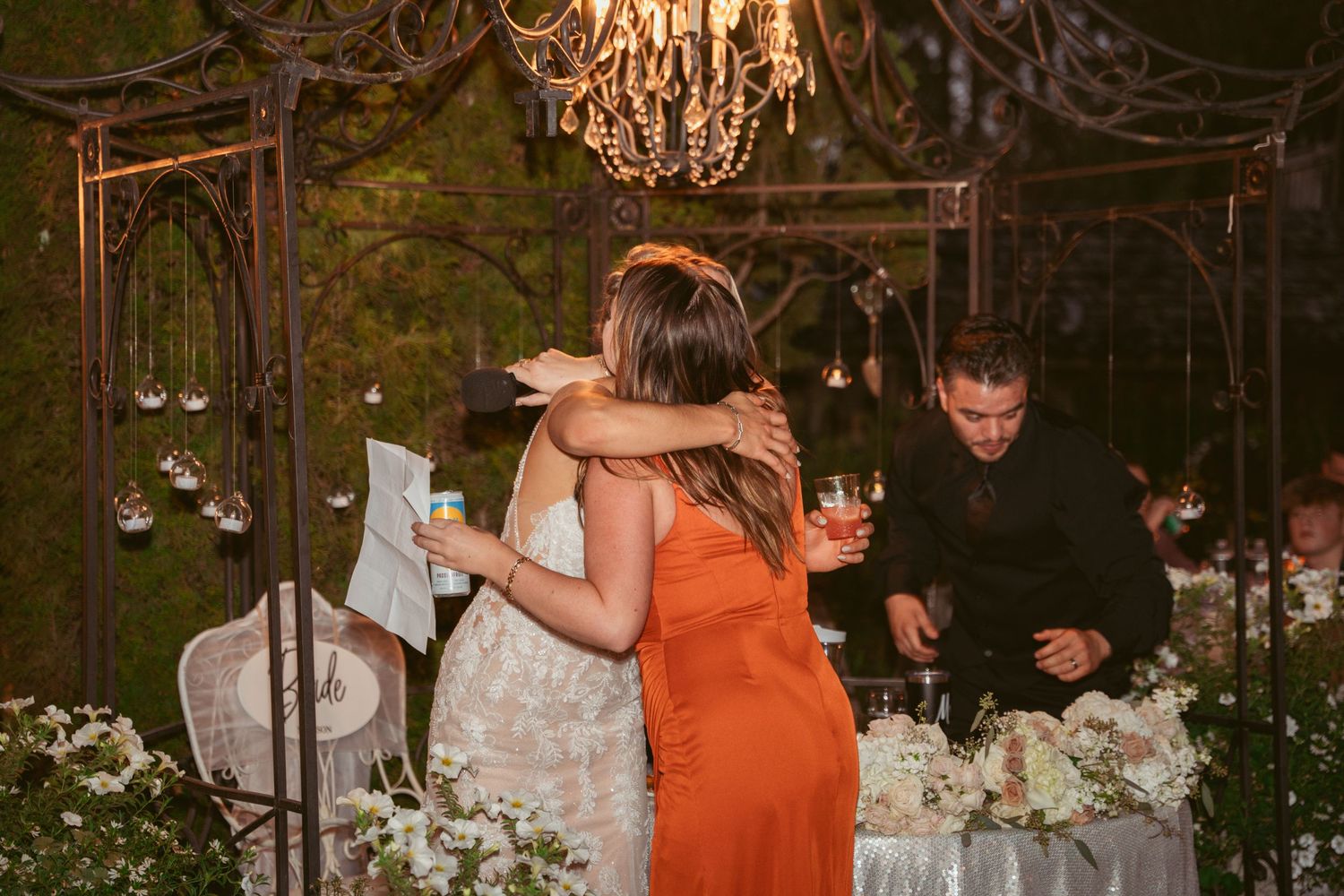Wedding celebration under an ornate chandelier with floral decorations at night.