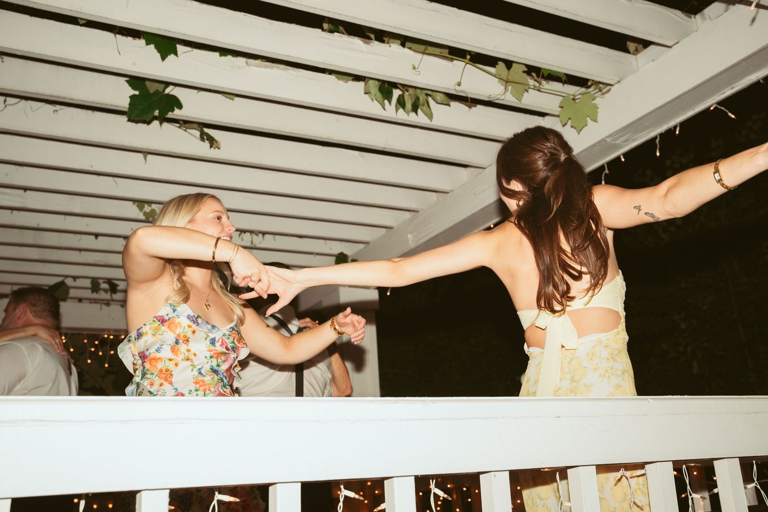 Two people dancing energetically under a white pergola at night.