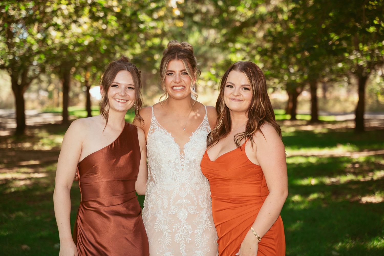 Wedding party in rust and orange colored dresses posing outdoors.
