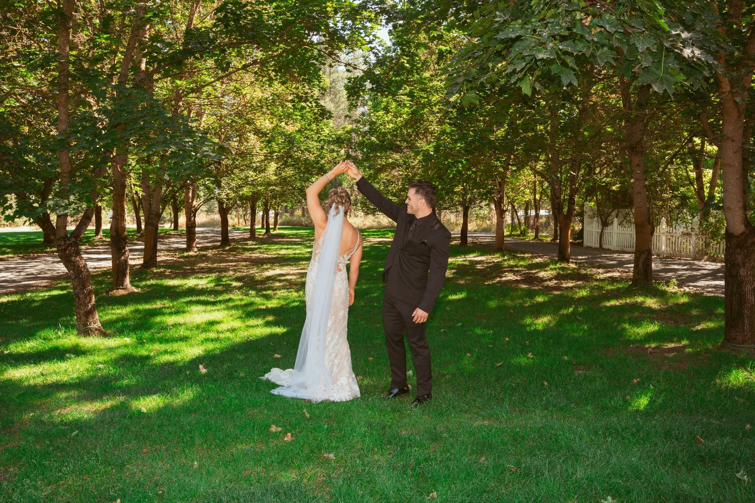 A couple shares a joyful moment together in a sunlit park with green trees creating a natural backdrop.