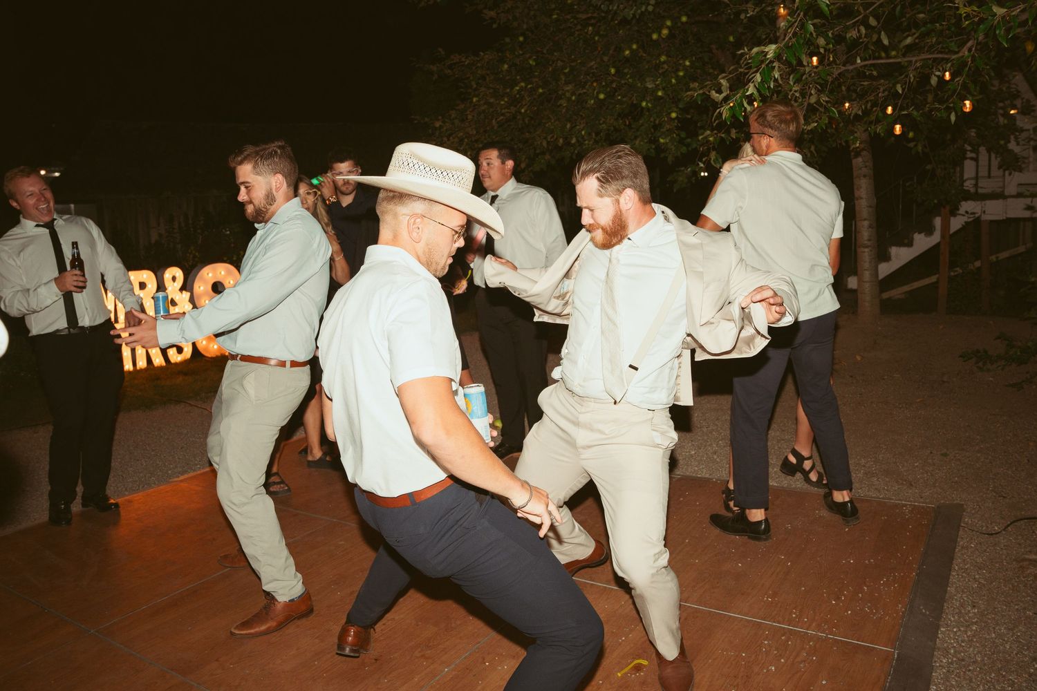 Wedding guests dancing enthusiastically in cowboy hats at outdoor reception.