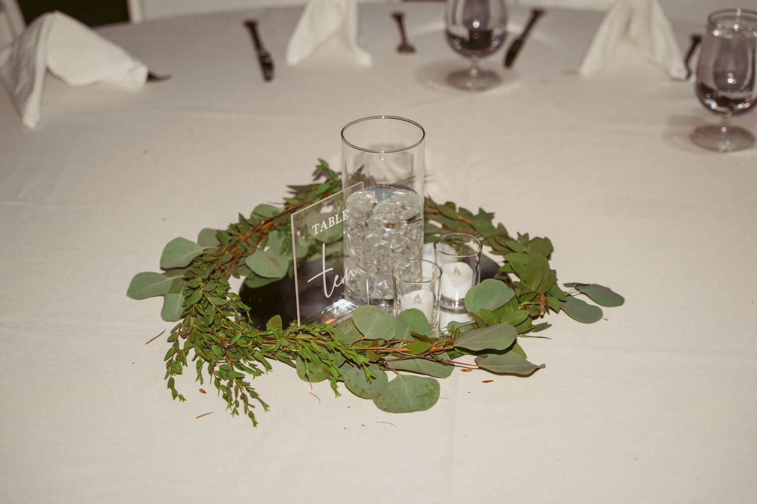 Decorative green eucalyptus leaves and branches arranged as table centerpieces for an elegant dining setting.