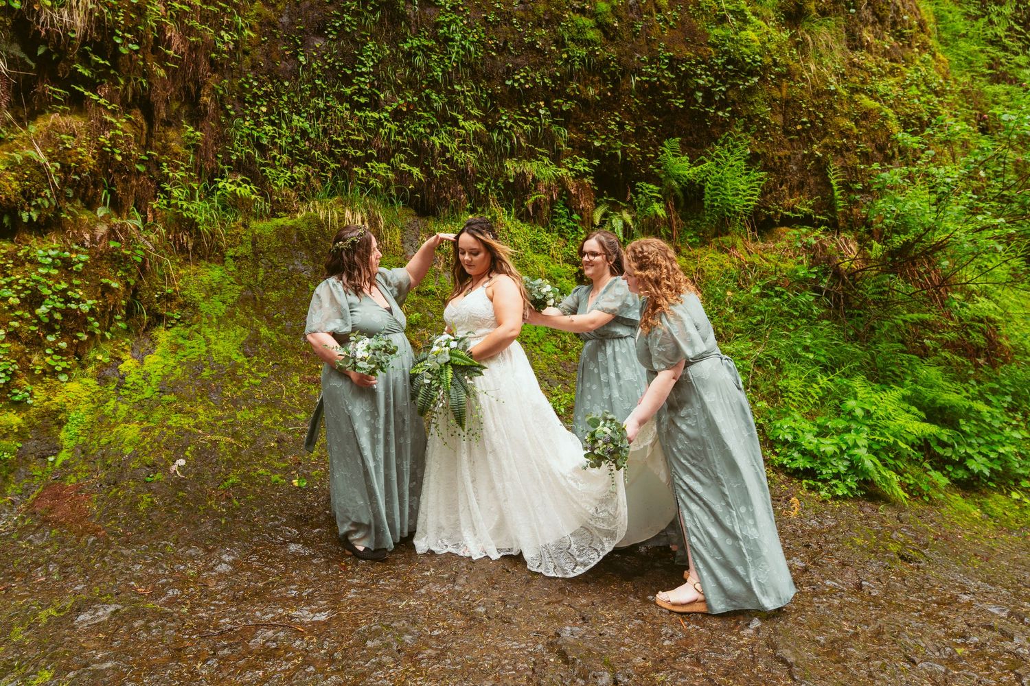Wedding party members gather by a waterfall for outdoor photos in sage and white dresses.