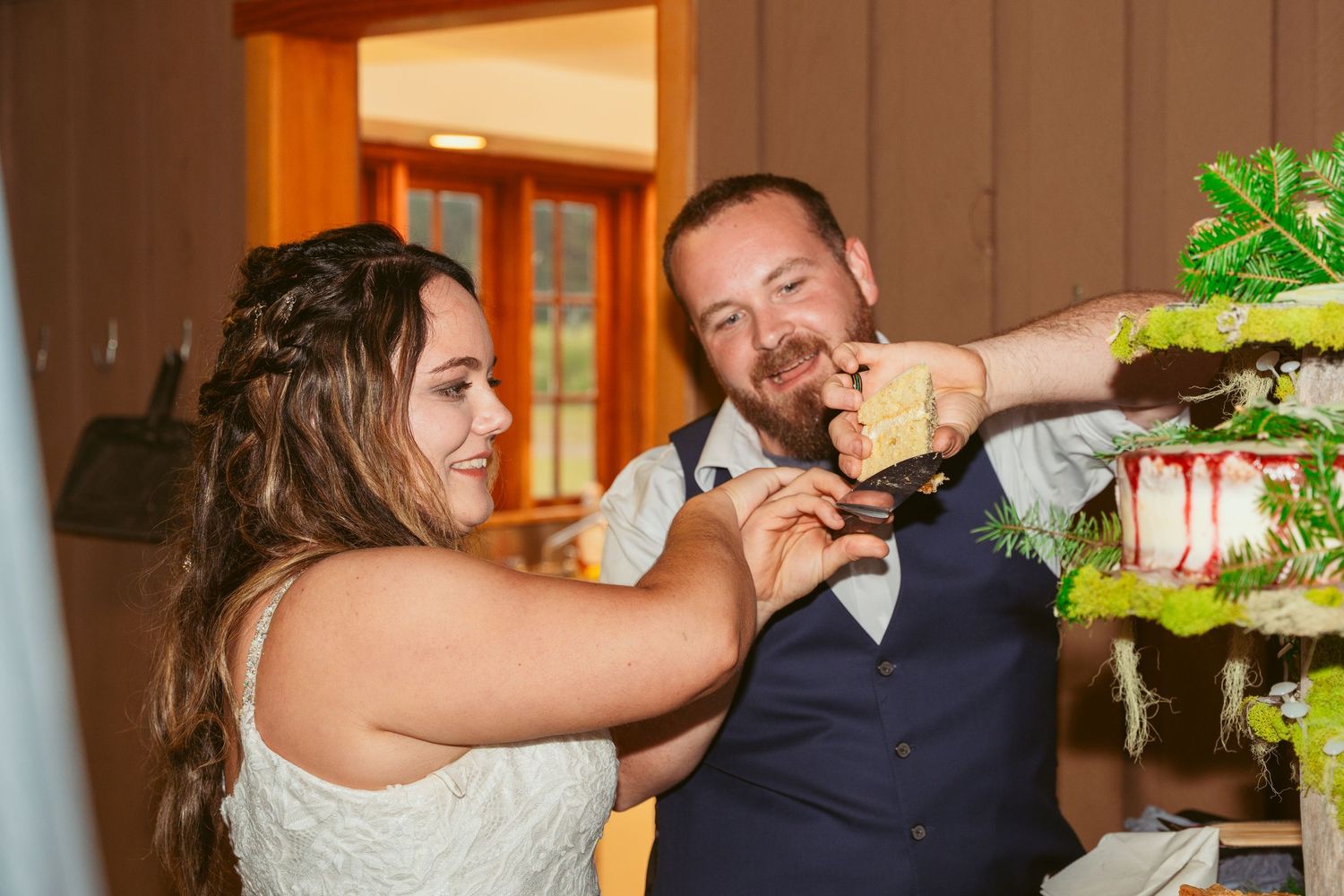 Wedding couple sharing cake with playful expressions at their indoor reception.