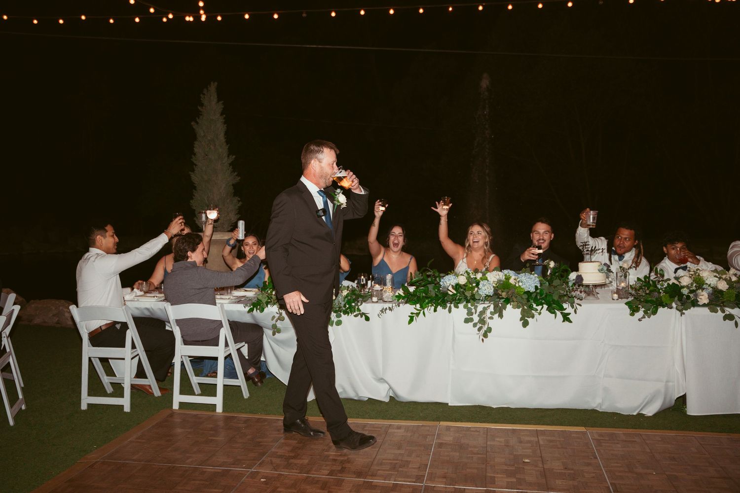 Evening wedding reception setup with string lights and white folding chairs.