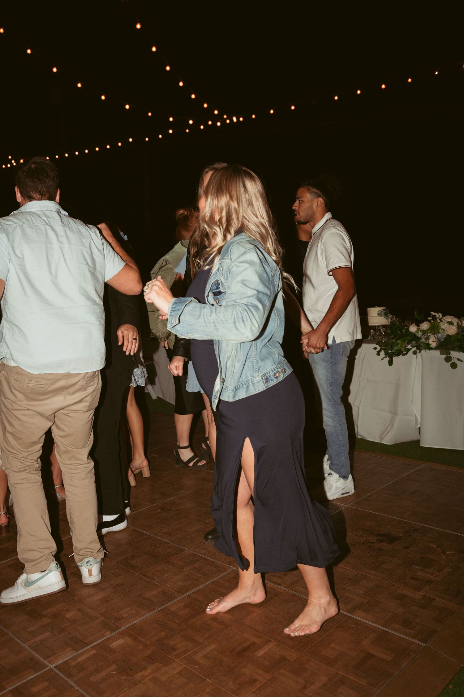 Wedding guests dancing barefoot on wooden dance floor during evening celebration.