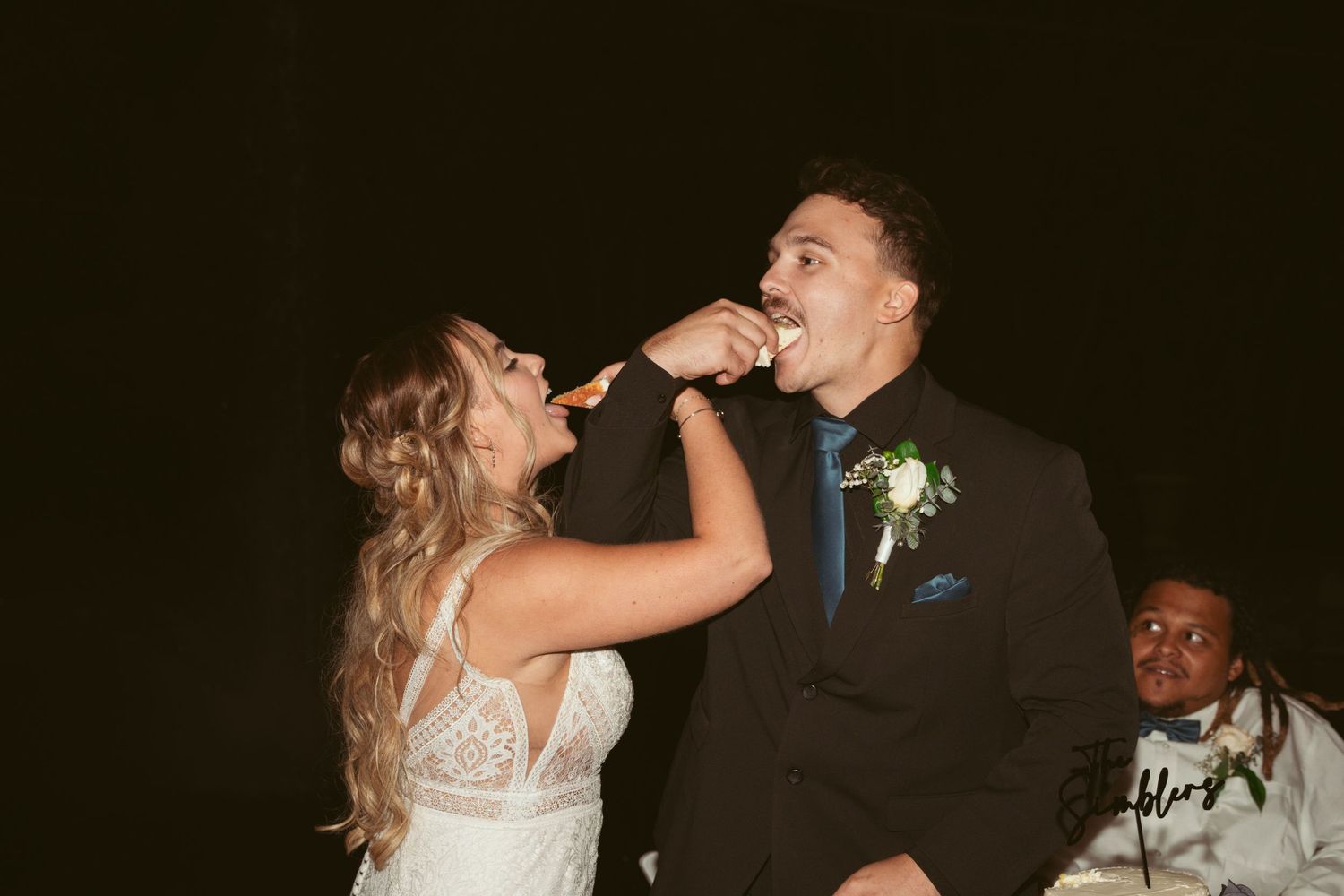 A bride and groom share a celebratory drink together at their wedding reception in a dark, candlelit setting.