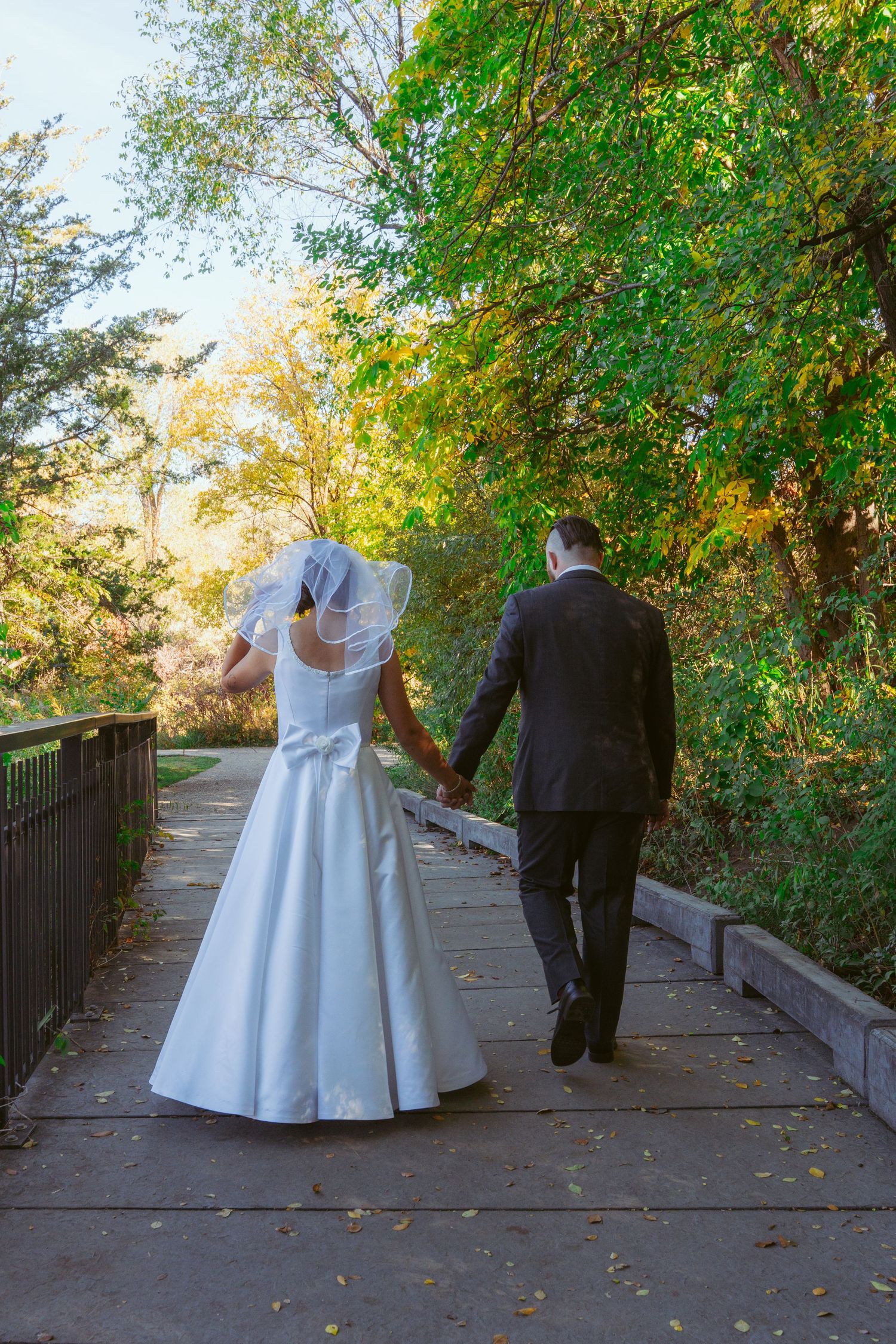 A couple walks along a tree-lined path during an autumn wedding photoshoot.