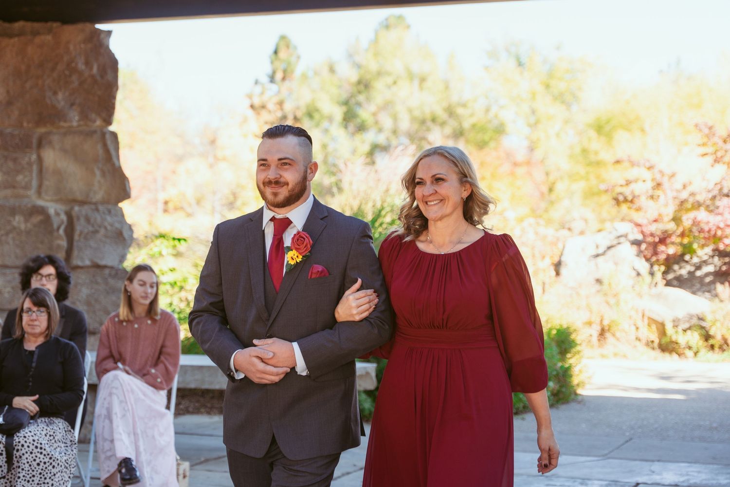 Wedding party members in burgundy and grey attire gather on a stone patio.