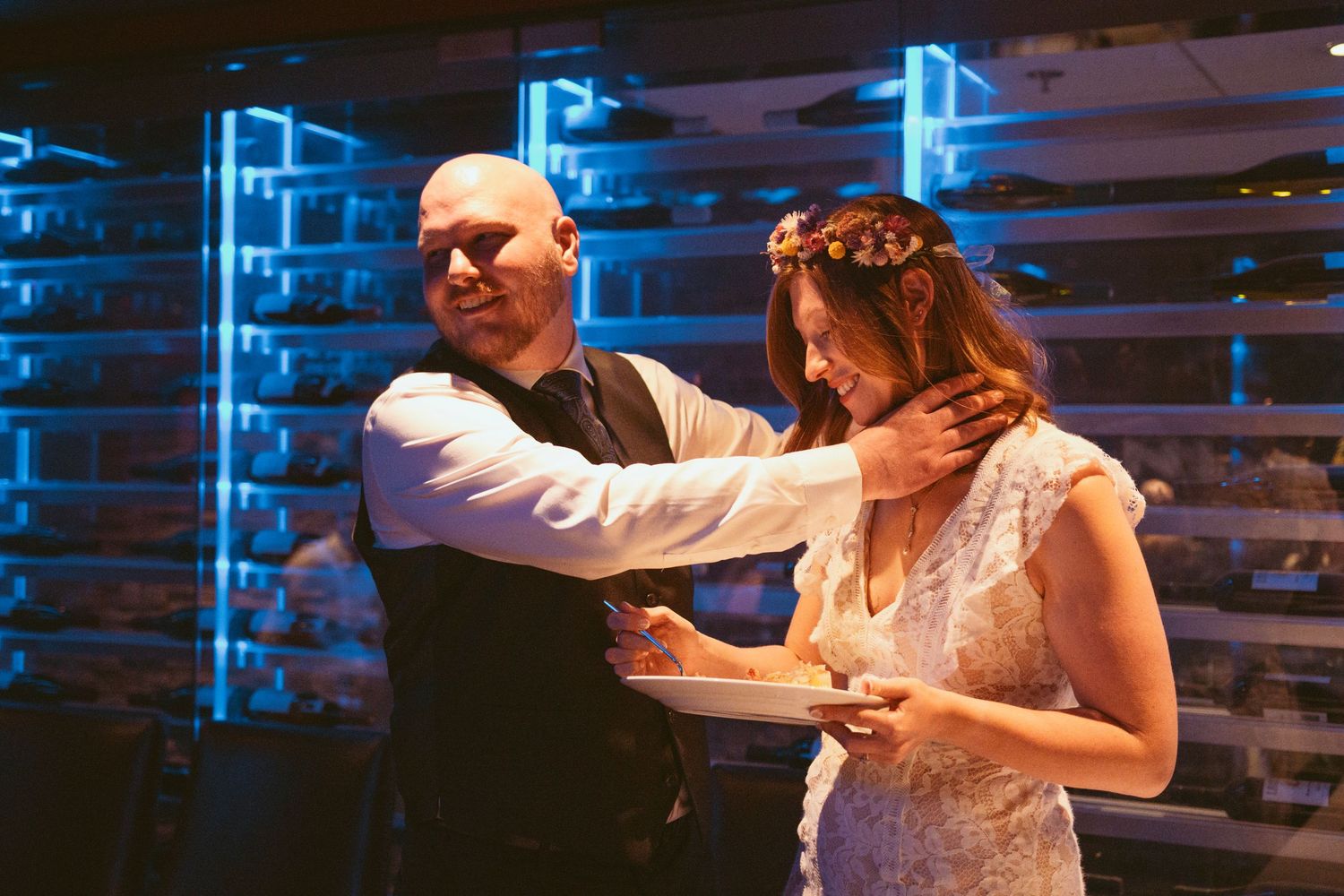 Wedding couple dancing under blue neon lights with wooden pallet wall backdrop.