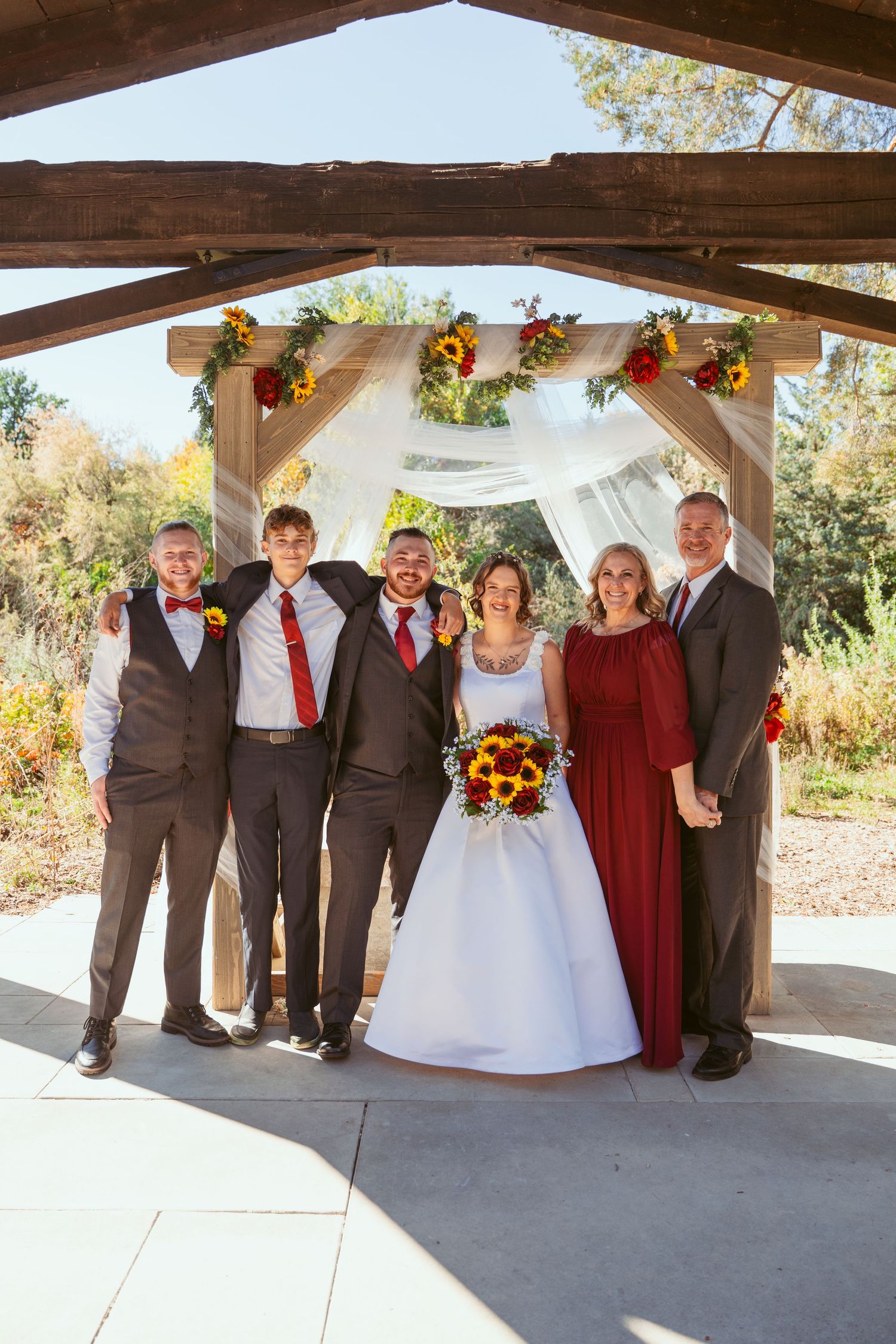 Wedding party poses under covered pavilion with burgundy and grey color scheme.