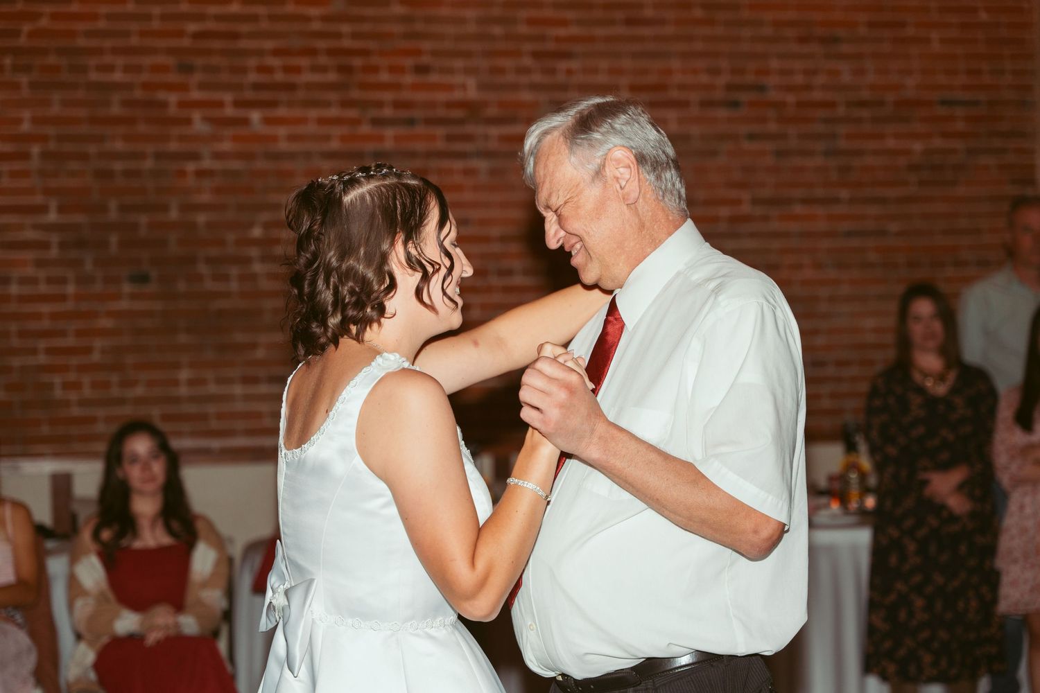 An emotional dance shared at a wedding reception with exposed brick walls and string lights.