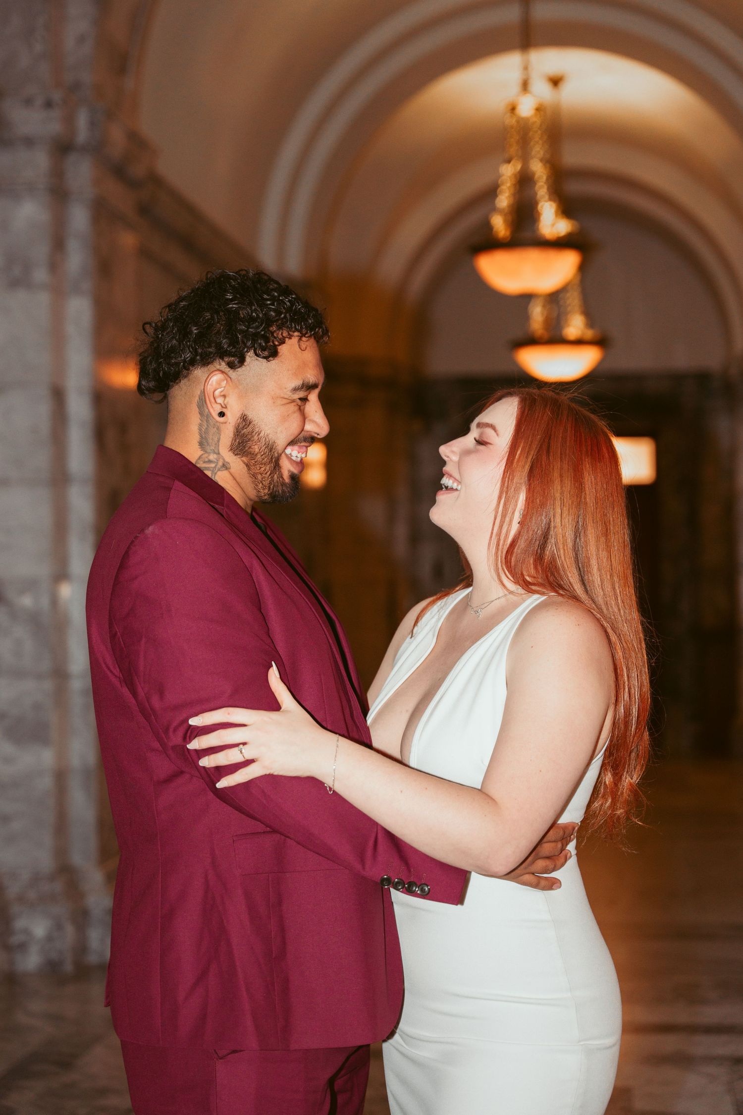 A couple shares an intimate moment in an elegant hallway with arched ceilings and warm lighting.