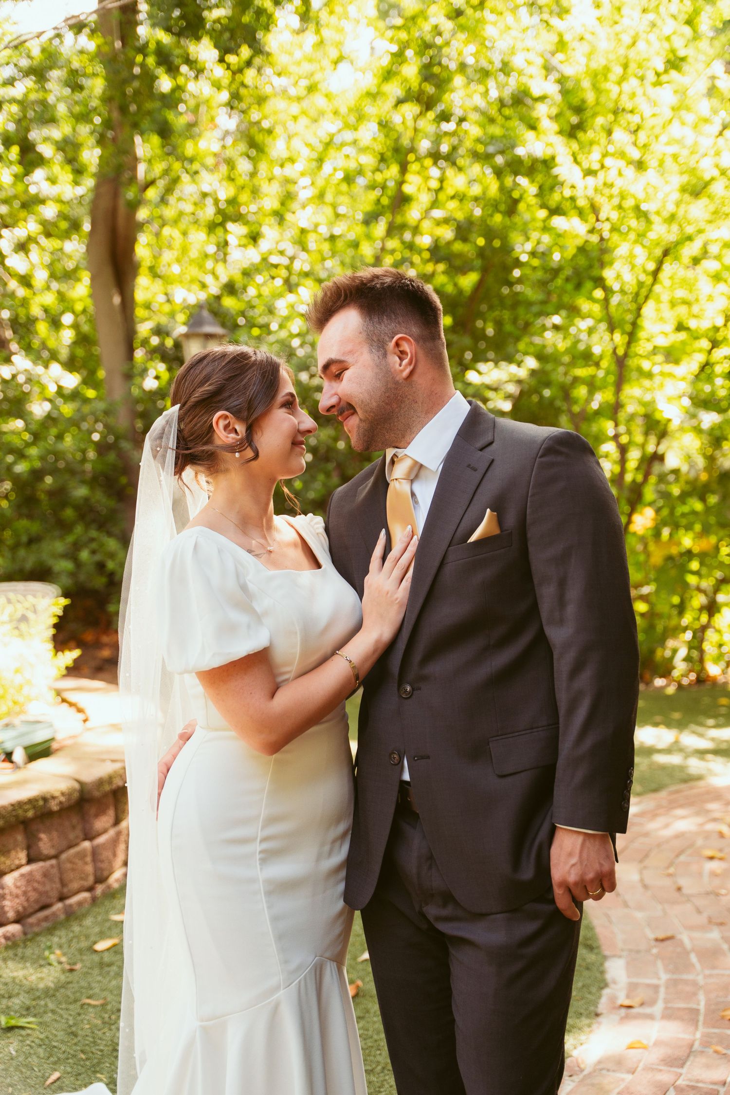 Sunlit wedding portraits capture tender moments between newlyweds in an outdoor garden setting.