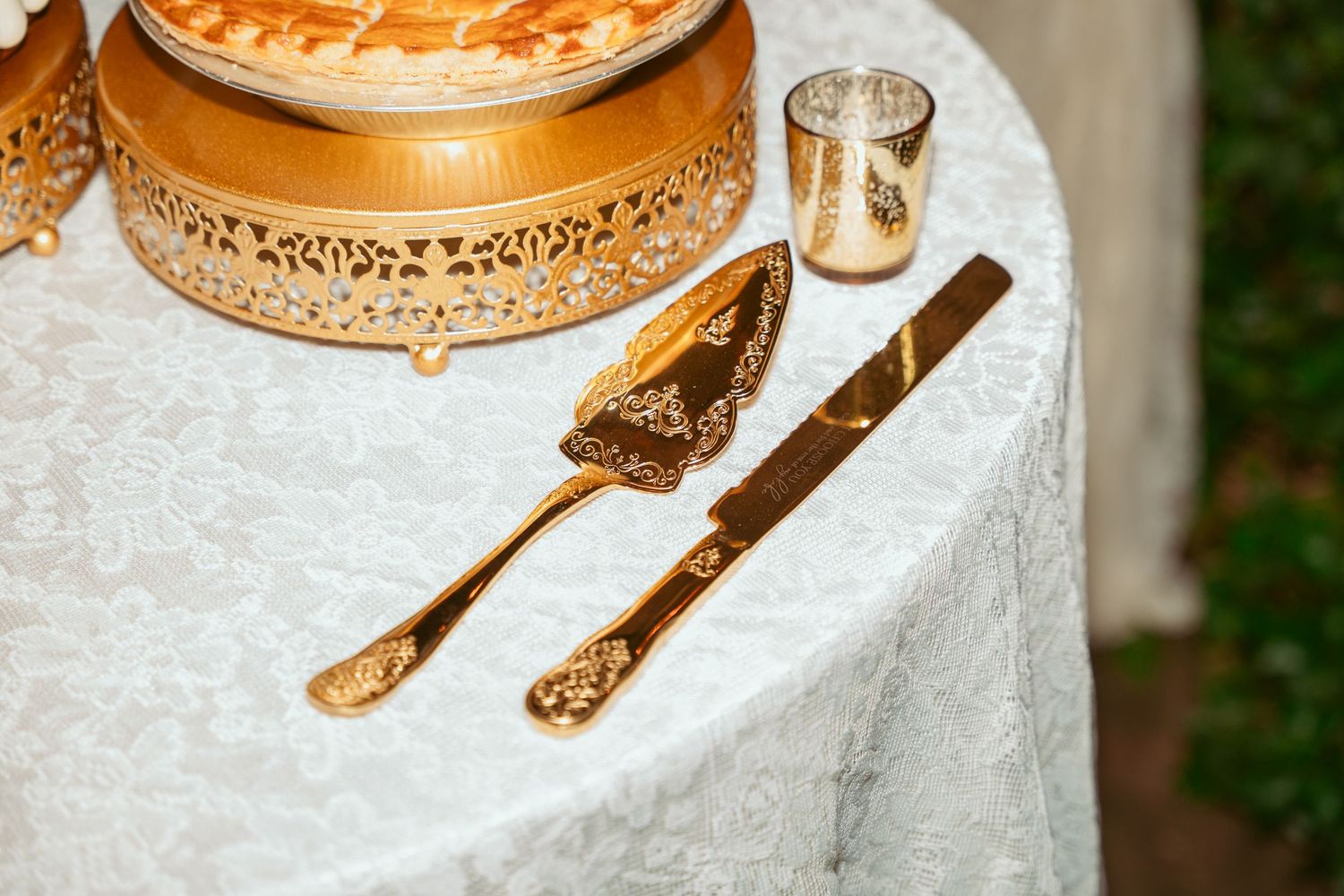 Close-up of ornate gold cake stands and serving utensils on white tablecloth.