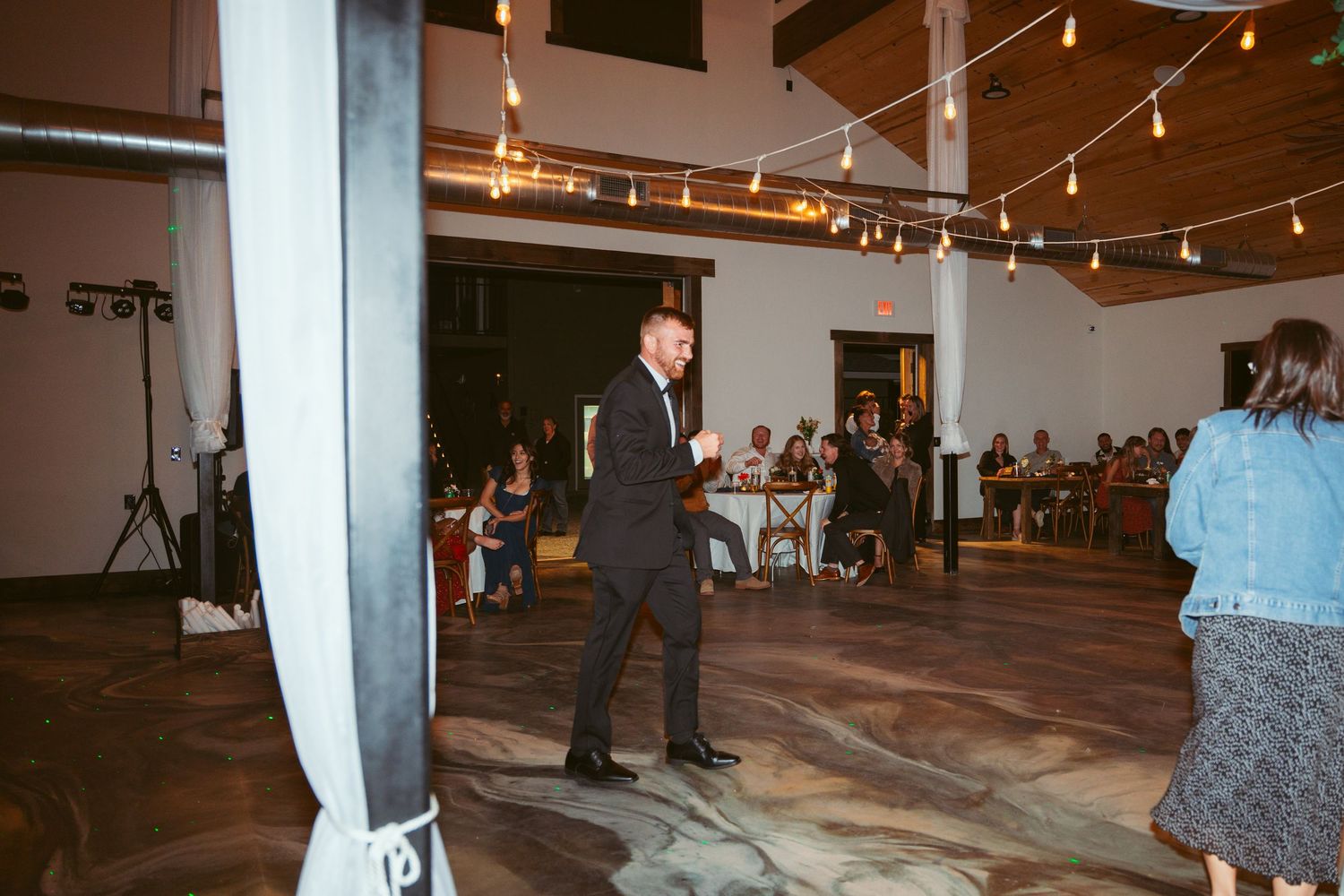 A reception venue with exposed beams and string lights during an evening celebration.