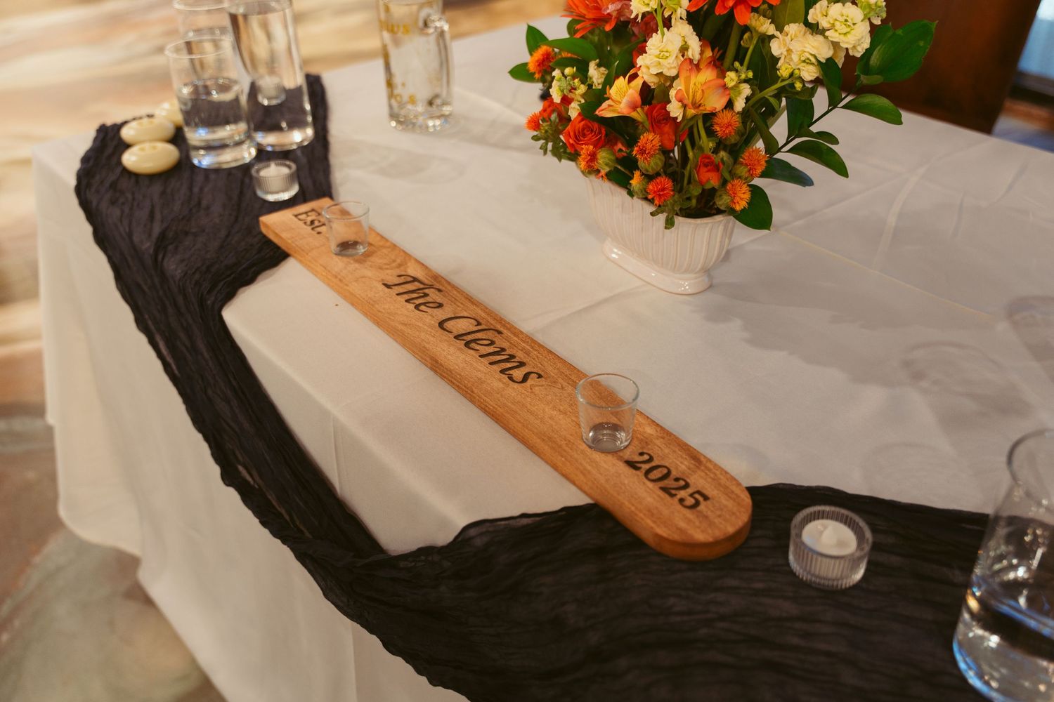 Wedding reception table with personalized wooden sign and black runner decor.