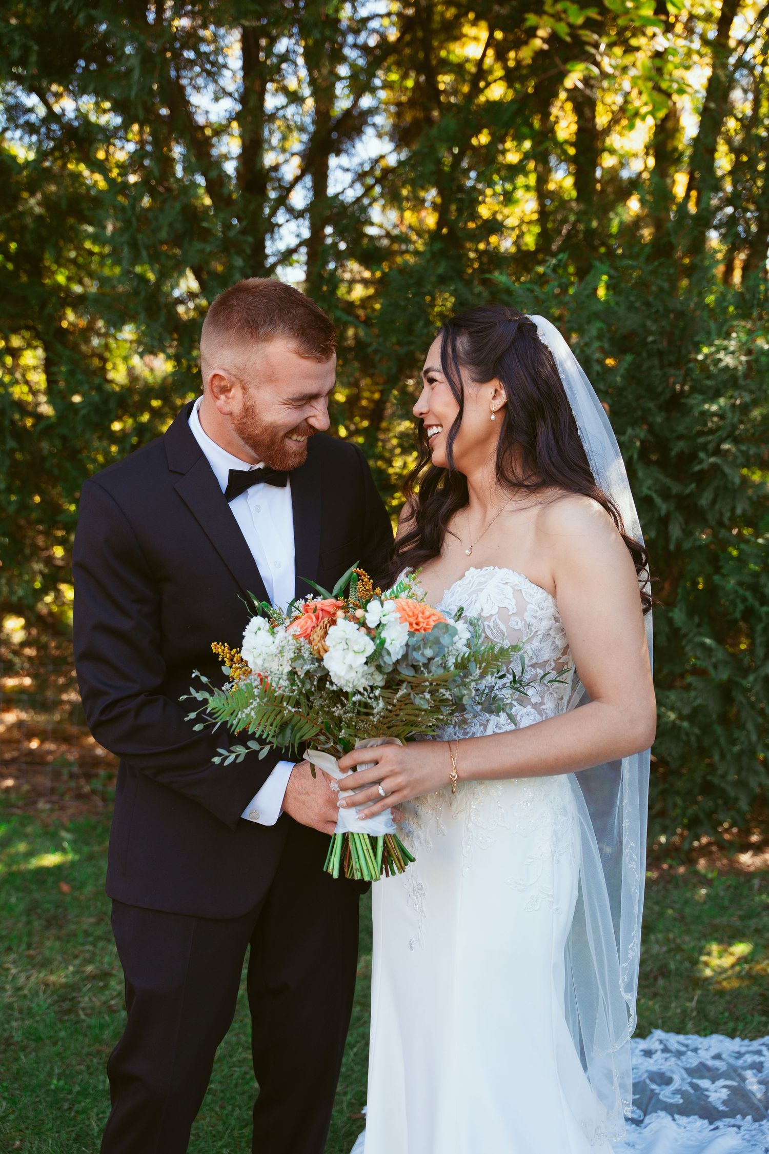 Joyful wedding couple shares a laugh while holding a beautiful bouquet of mixed flowers.