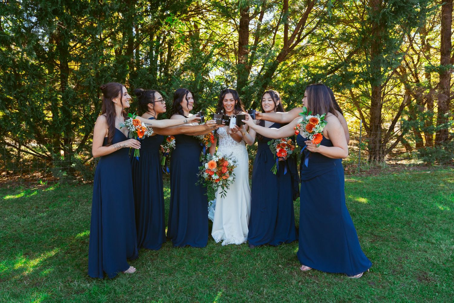 Bridal party in navy blue dresses poses playfully in circle formation outdoors.
