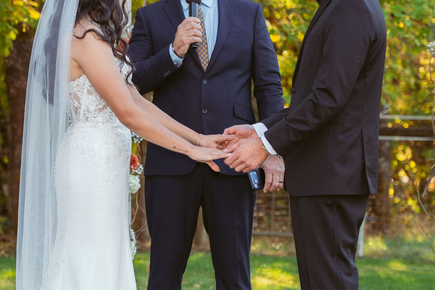 Close-up of joined hands during wedding ceremony under floral arch.