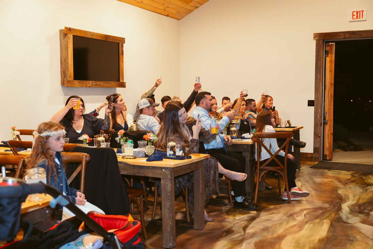 Wedding reception guests seated at tables in a rustic venue with wooden ceiling and warm lighting.