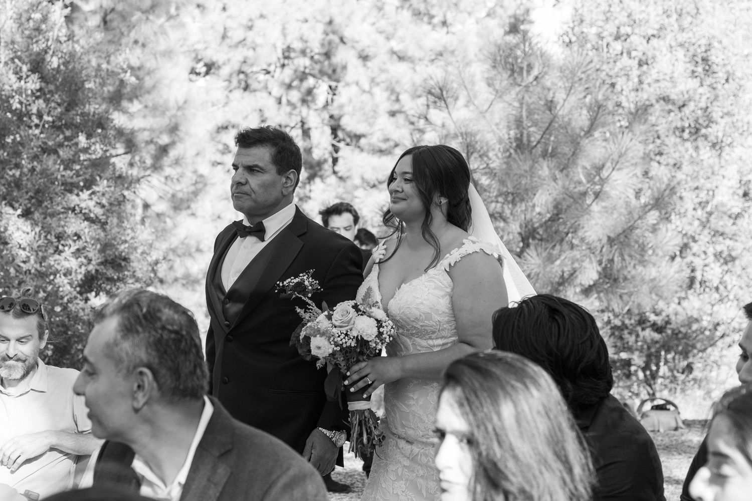 Black and white photo of wedding guests seated outdoors during a ceremony.