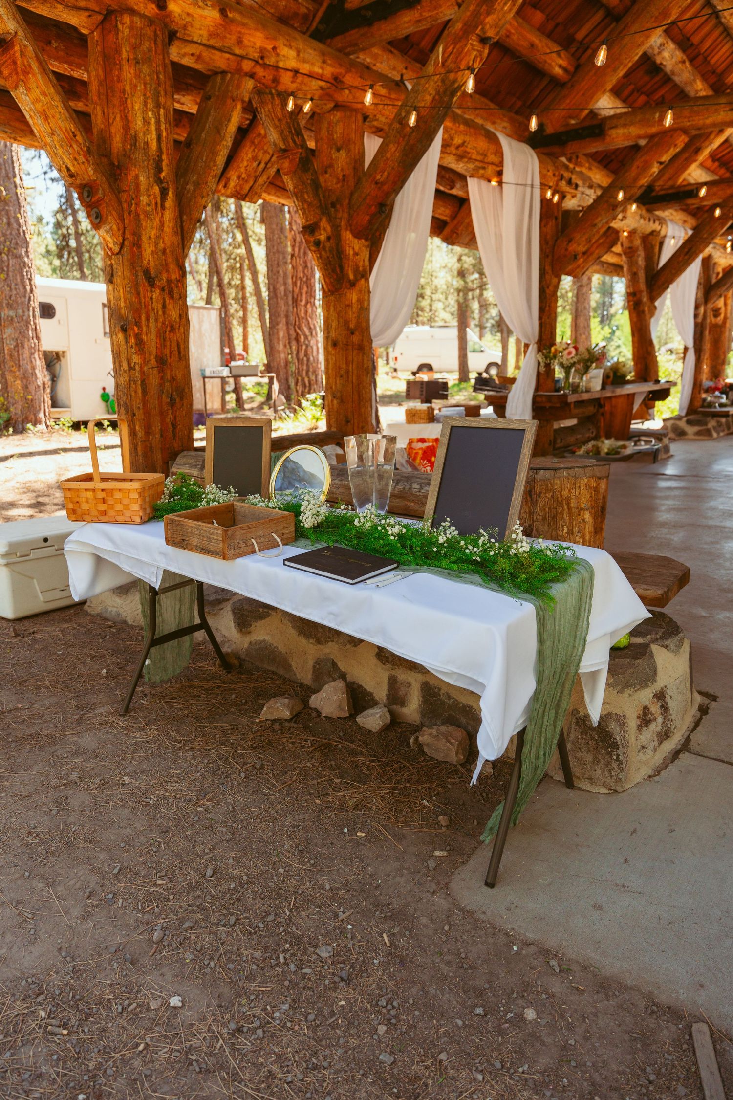 Long rustic wooden pavilion with white tablecloths and natural log supports for an outdoor event.