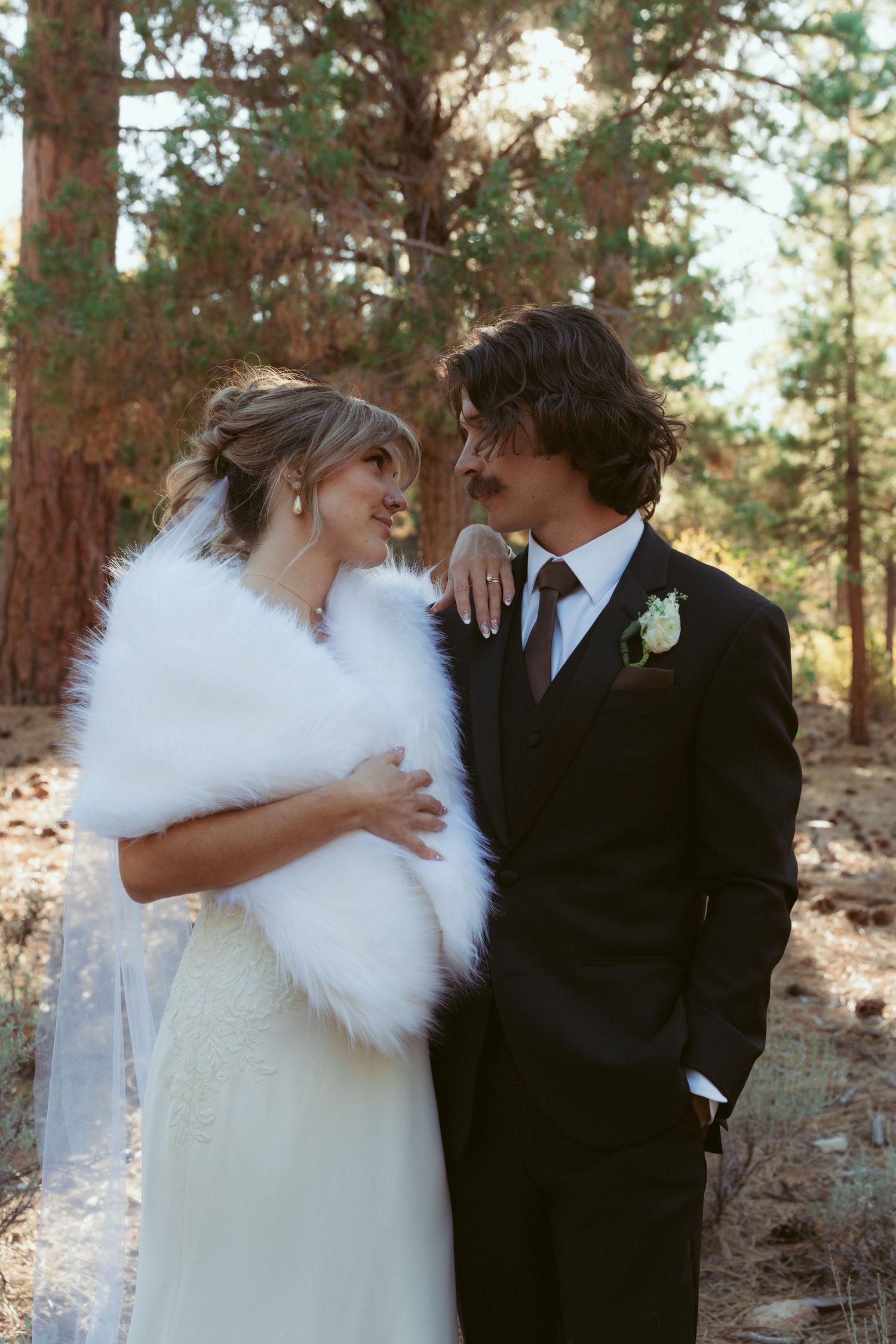 Newlyweds share intimate moments in a sunlit forest wearing classic black and white wedding attire.