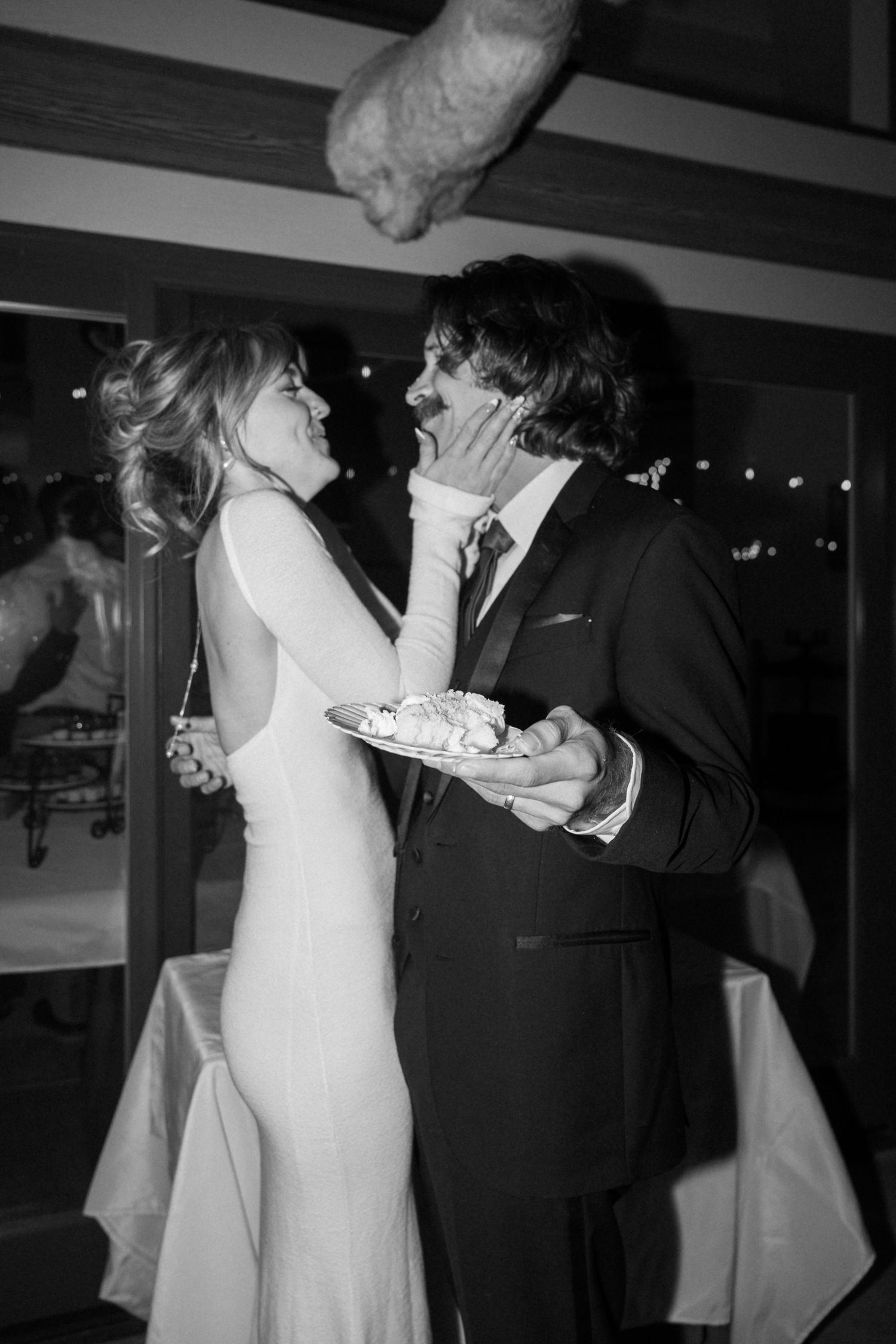 Couple laughs while feeding each other cake during wedding reception festivities.