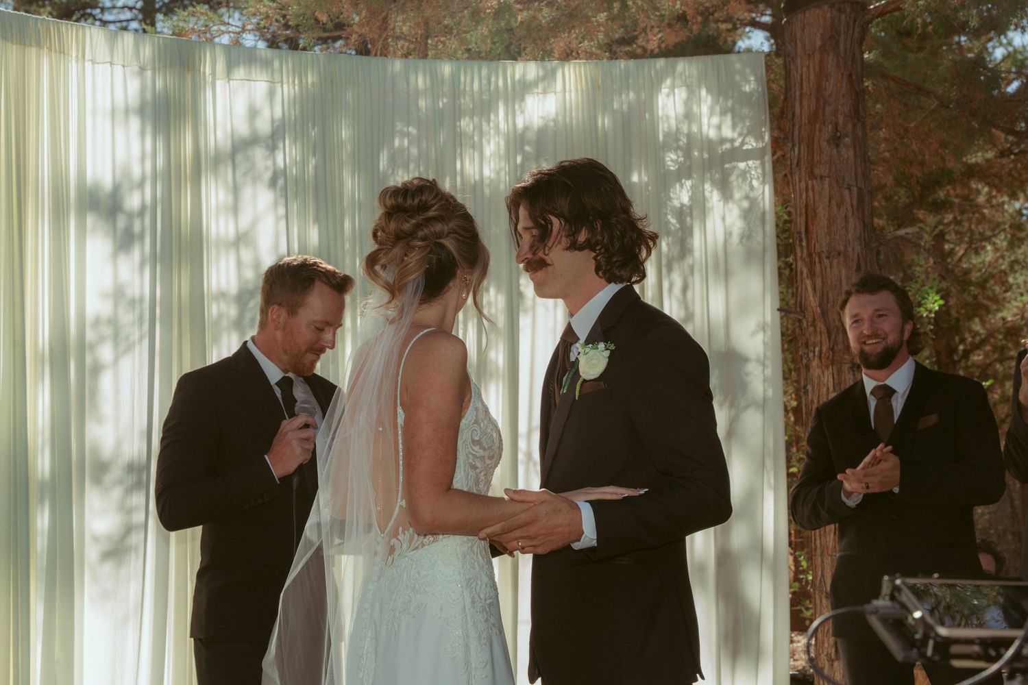 Wedding ceremony procession taking place under natural pine tree canopy.