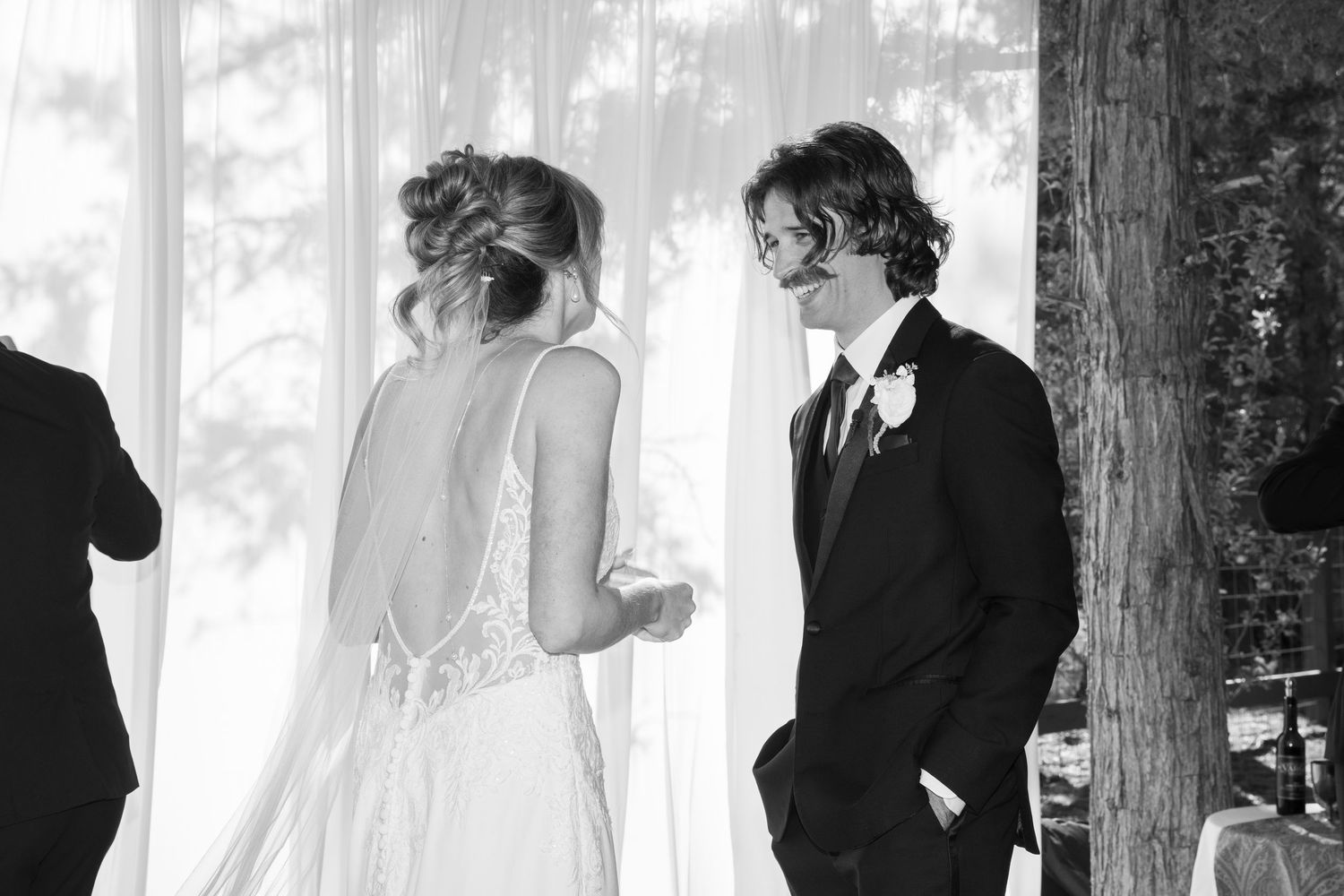 A black and white wedding photo showing a couple in an intimate moment with soft lighting and trees in background.