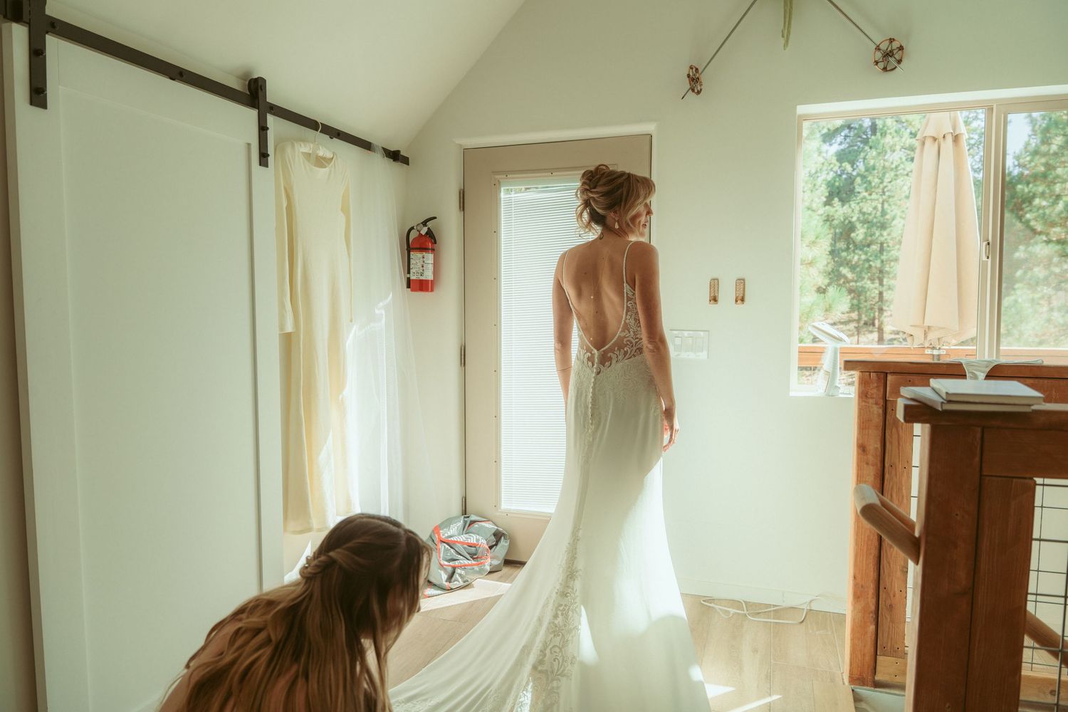 A sunlit room with hardwood floors shows wedding dress preparations from various angles.
