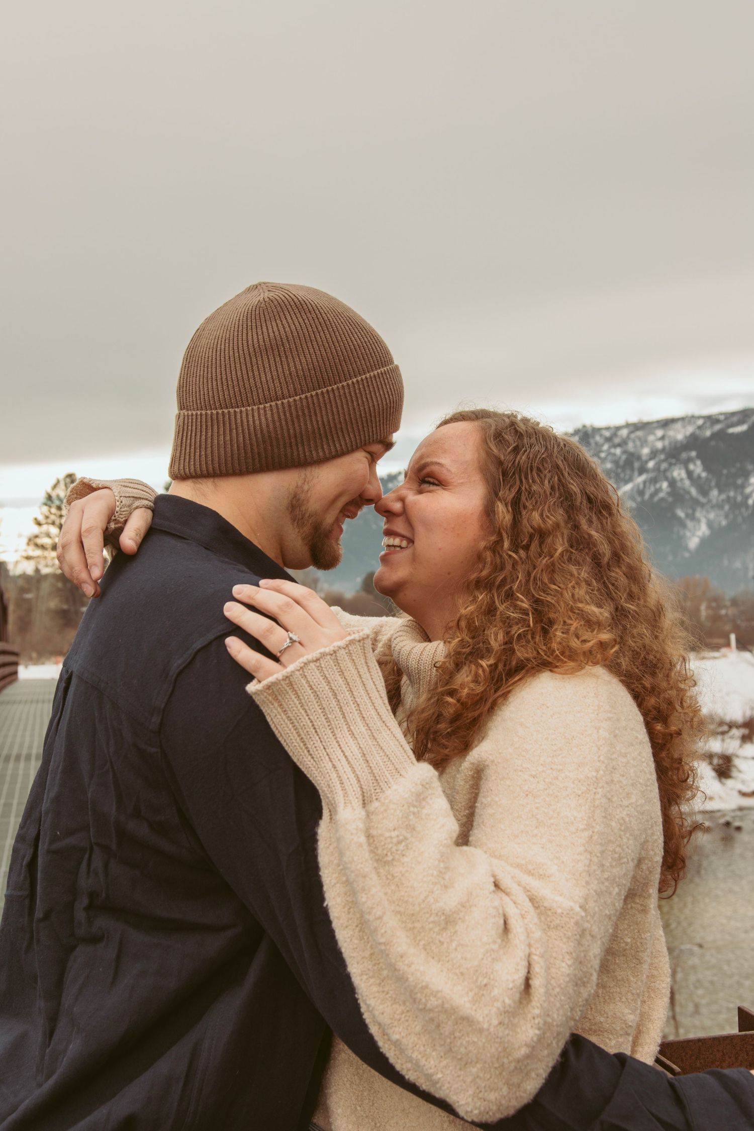 Couple sharing a playful romantic moment in a snowy mountain landscape wearing winter clothing.