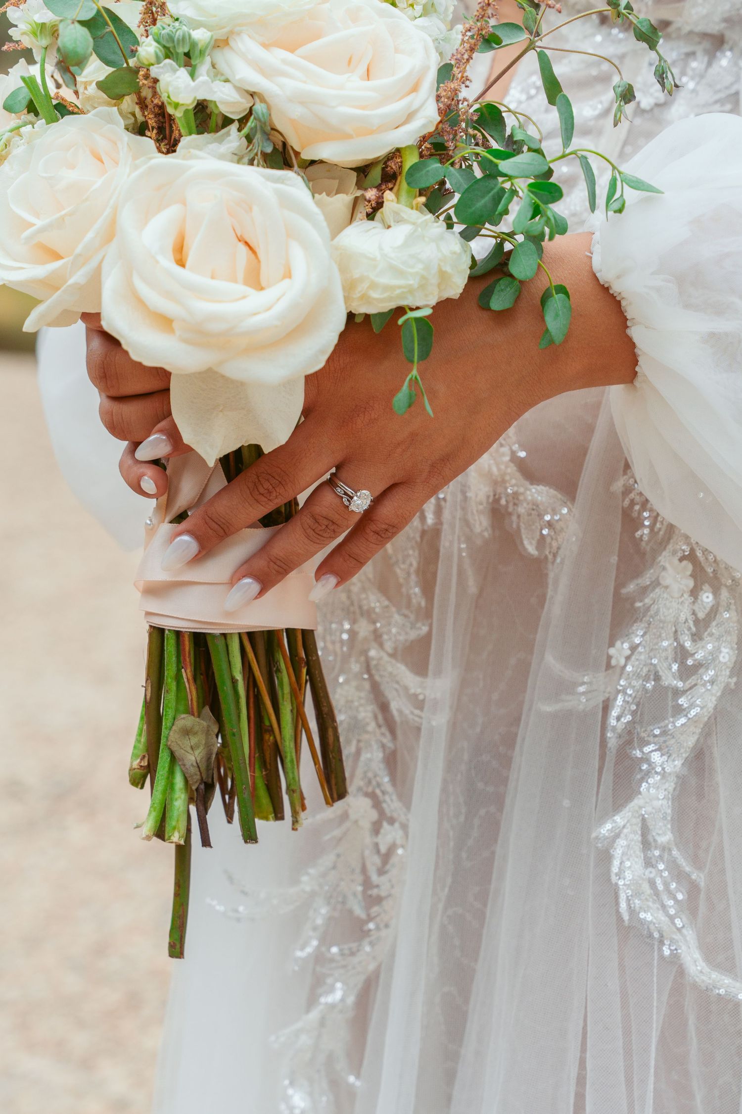 Close-up of bridal bouquets with cream roses and greenery against white lace dresses.
