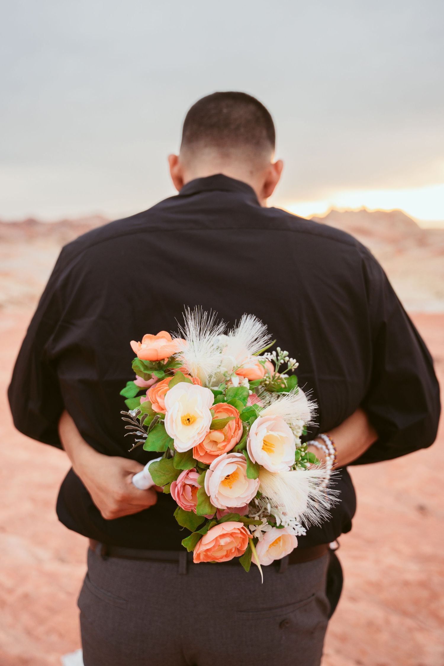 Close-up of coral and white wedding bouquet held against black attire.