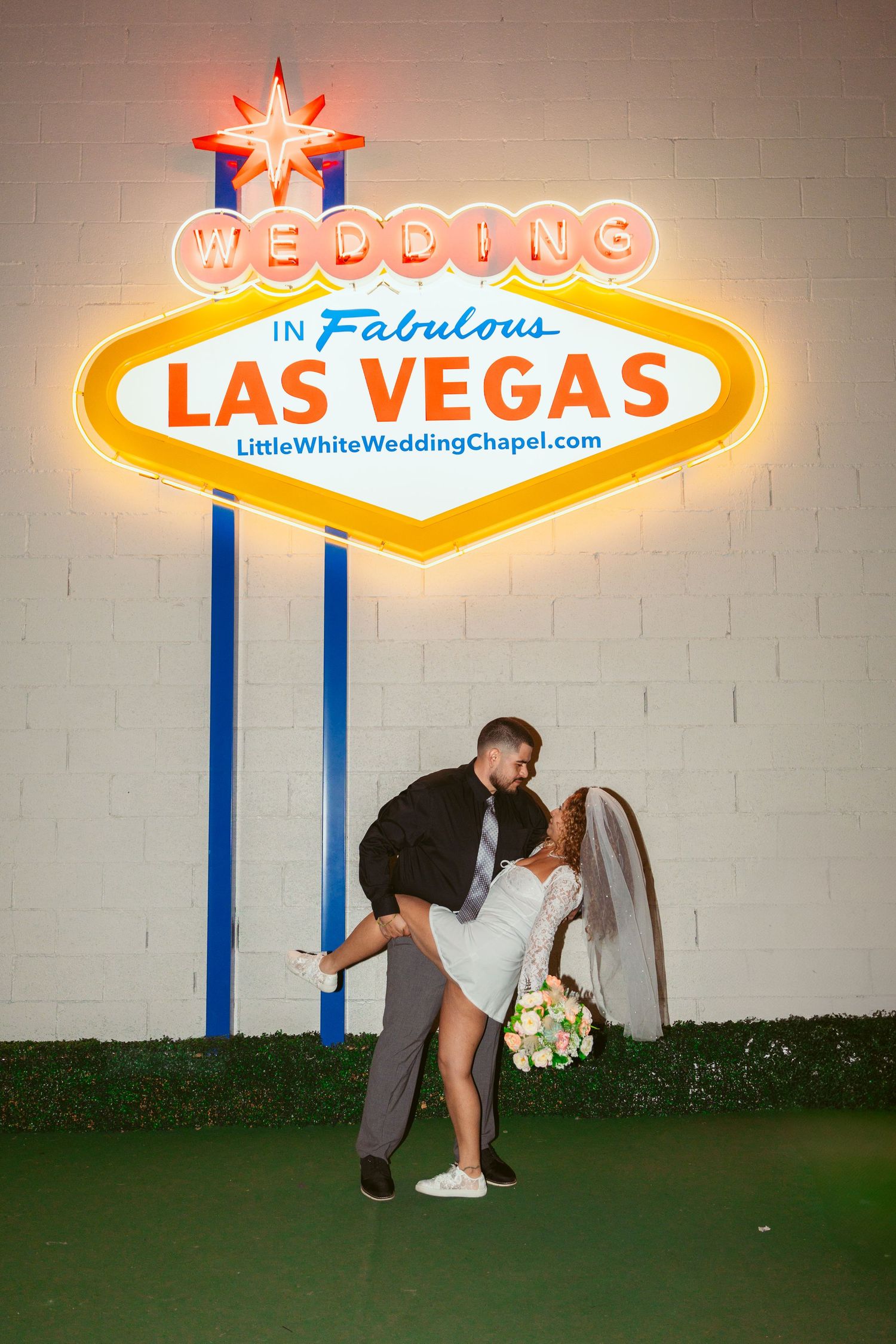 A romantic moment captured beneath the iconic Las Vegas sign at night.