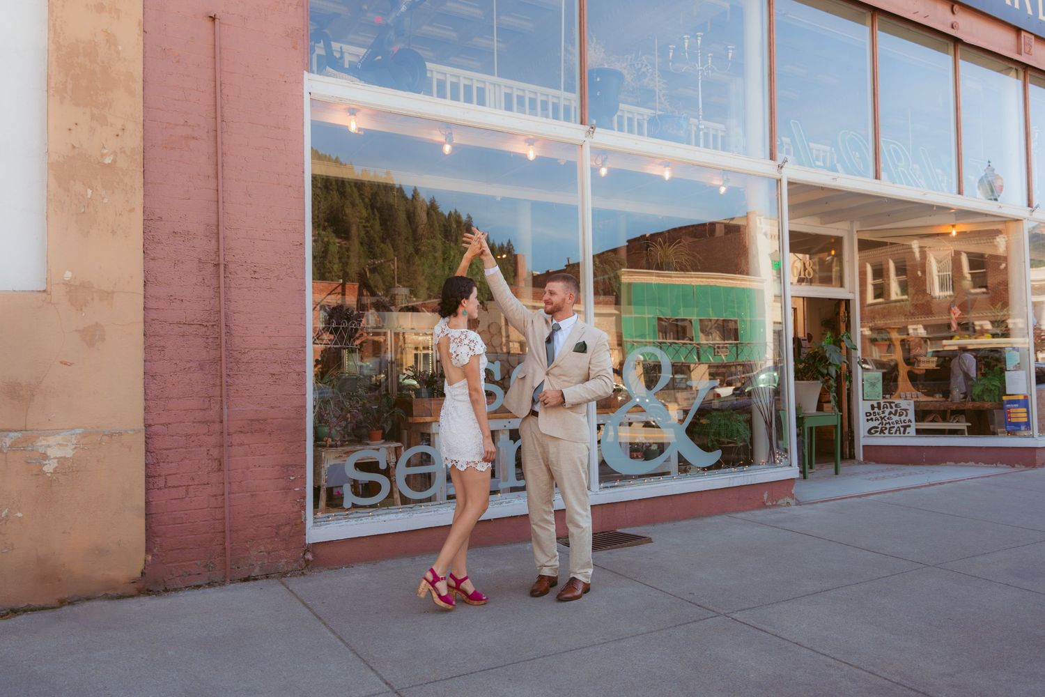 Couple in formal wear posing playfully against storefront windows.